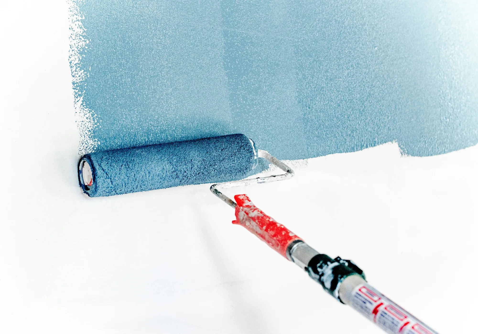 A roller applying fresh blue paint to a white wall